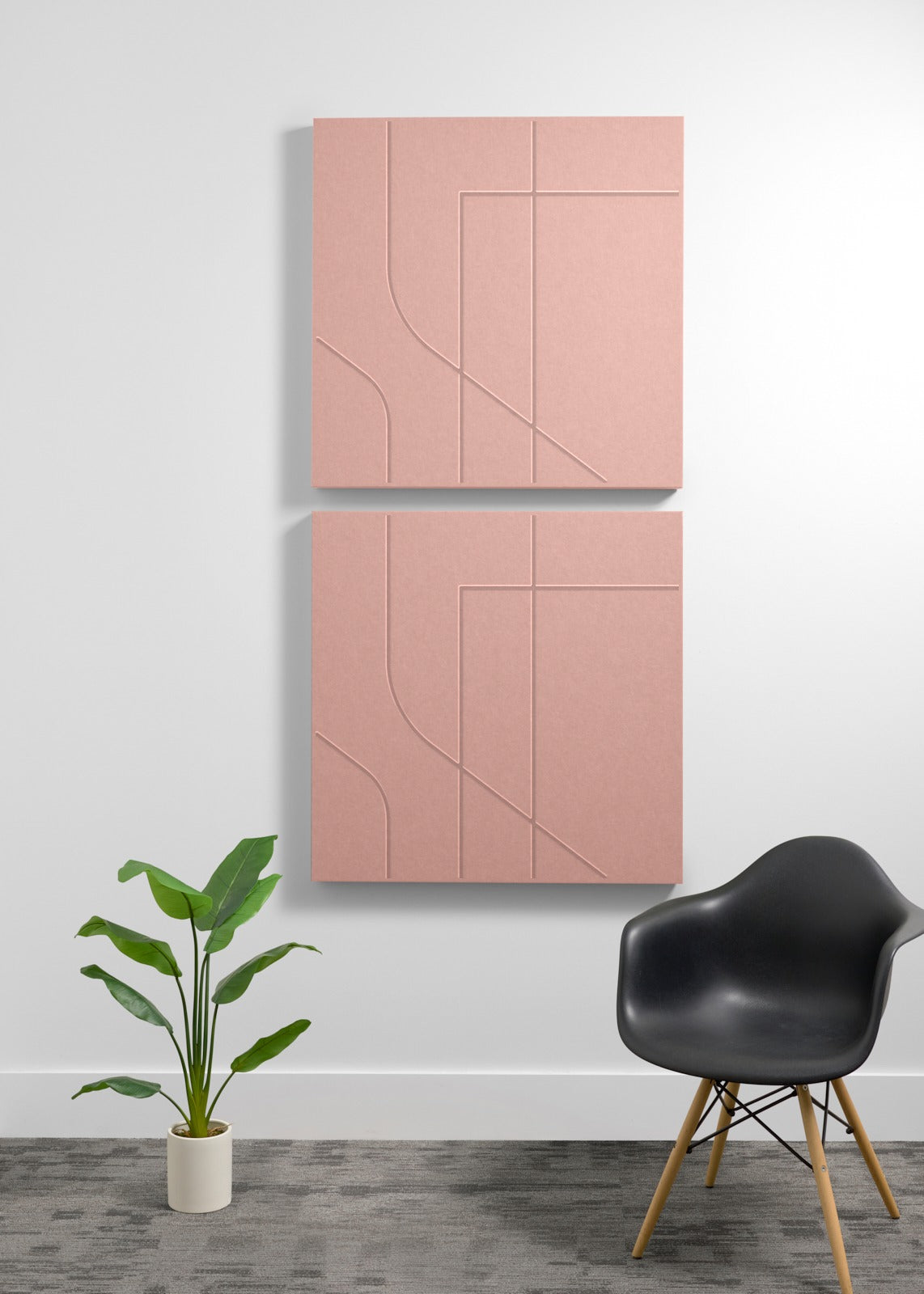Two coral pink square wall-mounted panels with engraving on a white wall with a black chair and plant in the foreground.