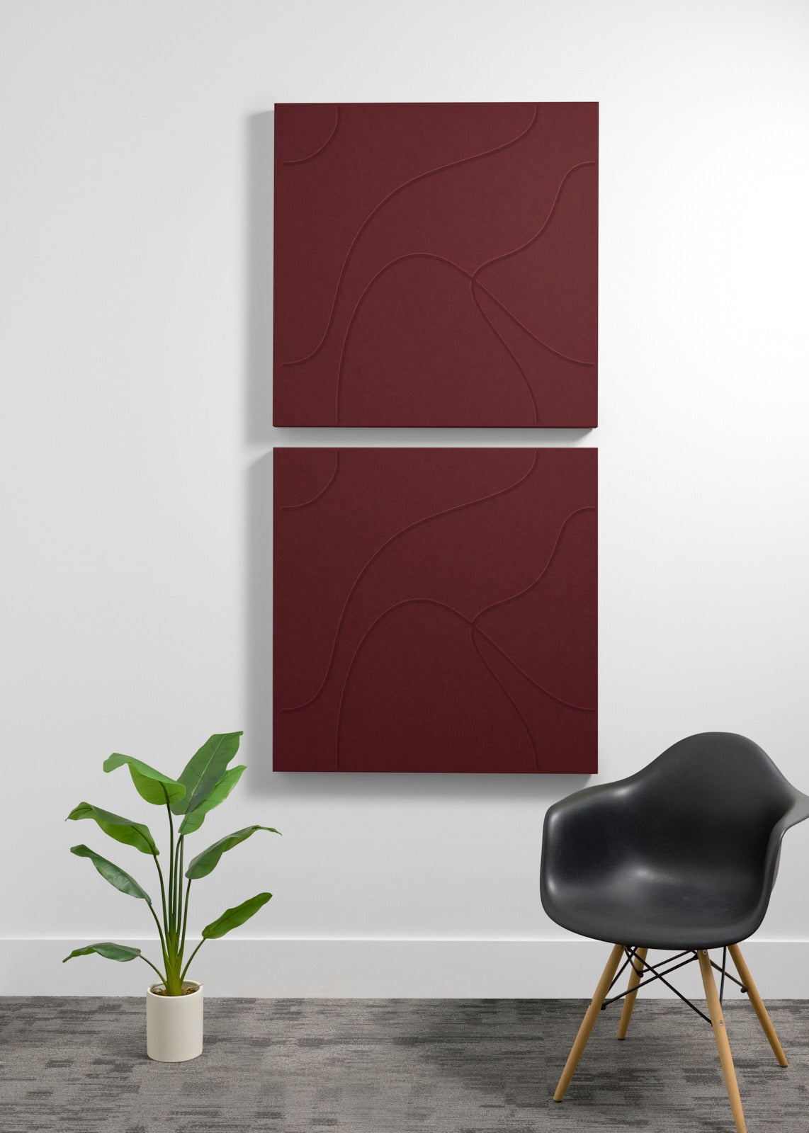 Two stacked burgundy acoustic panels with embossed wave patterns mounted on wall above chair and plant.