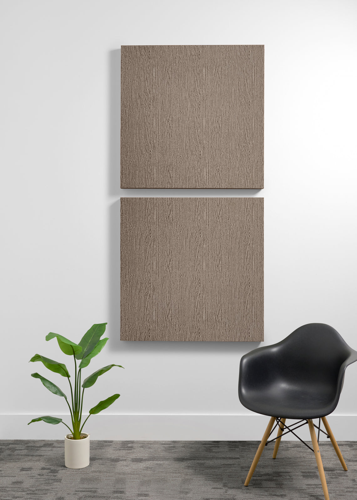 Two square dark wood wall art panels hanging vertically on a white wall in a modern room setting, with a black chair and a potted green plant below.