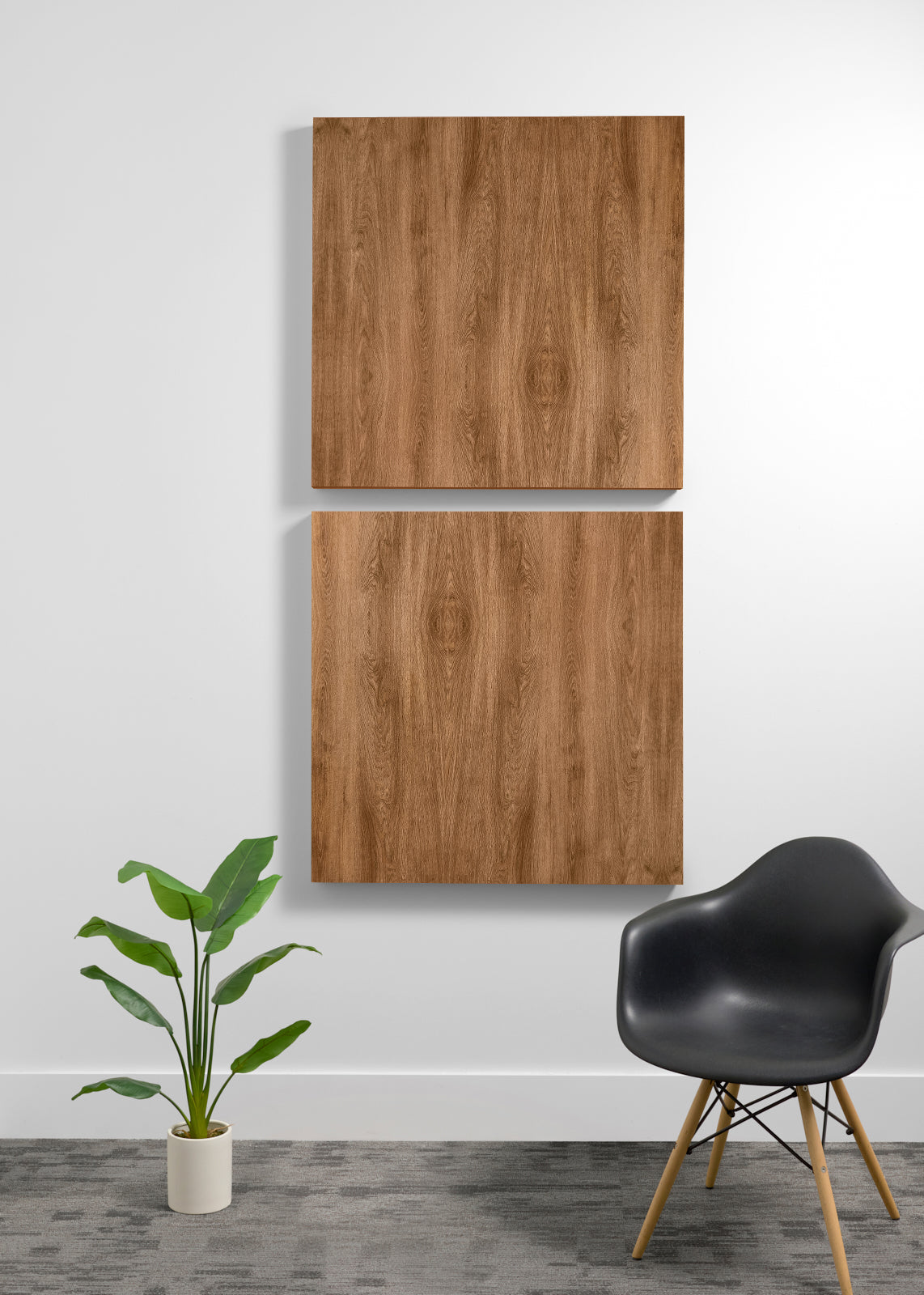 Two square wood wall art panels hanging vertically on a white wall in a modern room setting, with a black chair and a potted green plant below.