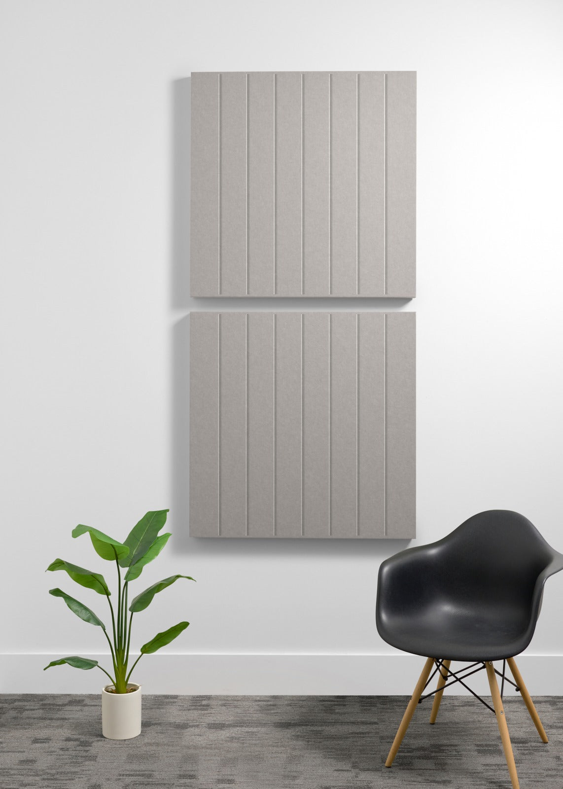 Two large gray acoustic wall panels with vertical grooves mounted on white wall above black chair and potted plant.