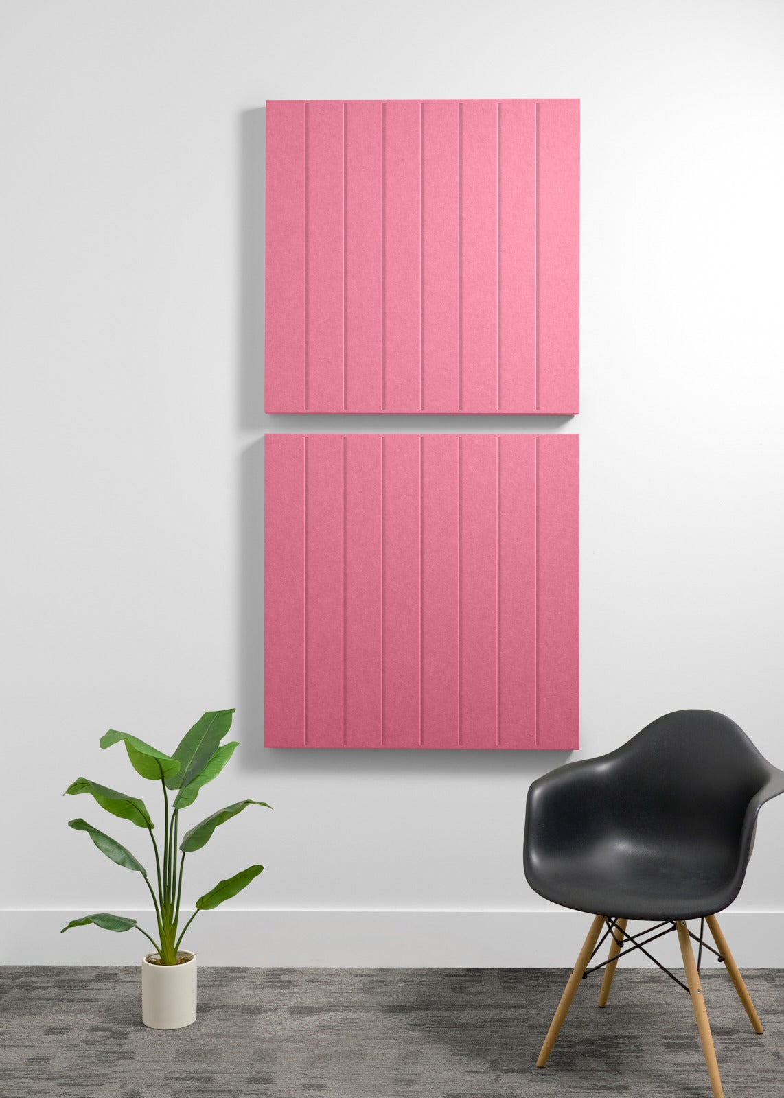 Two pink acoustic wall panels with vertical grooves mounted on a wall above a black chair and potted plant.