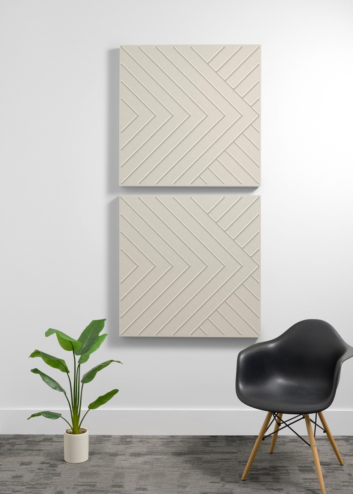 Two cream-colored square acoustic panels with engraved chevron pattern mounted on wall above chair and plant.