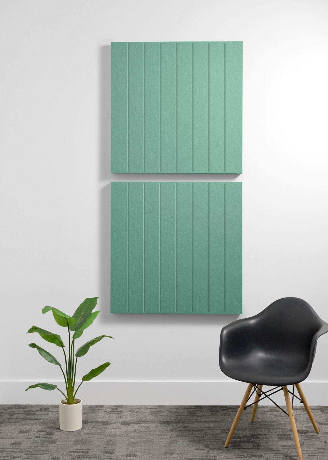 Two stacked sage green acoustic wall panels with vertical ribbed texture mounted on white wall above black chair and potted p
