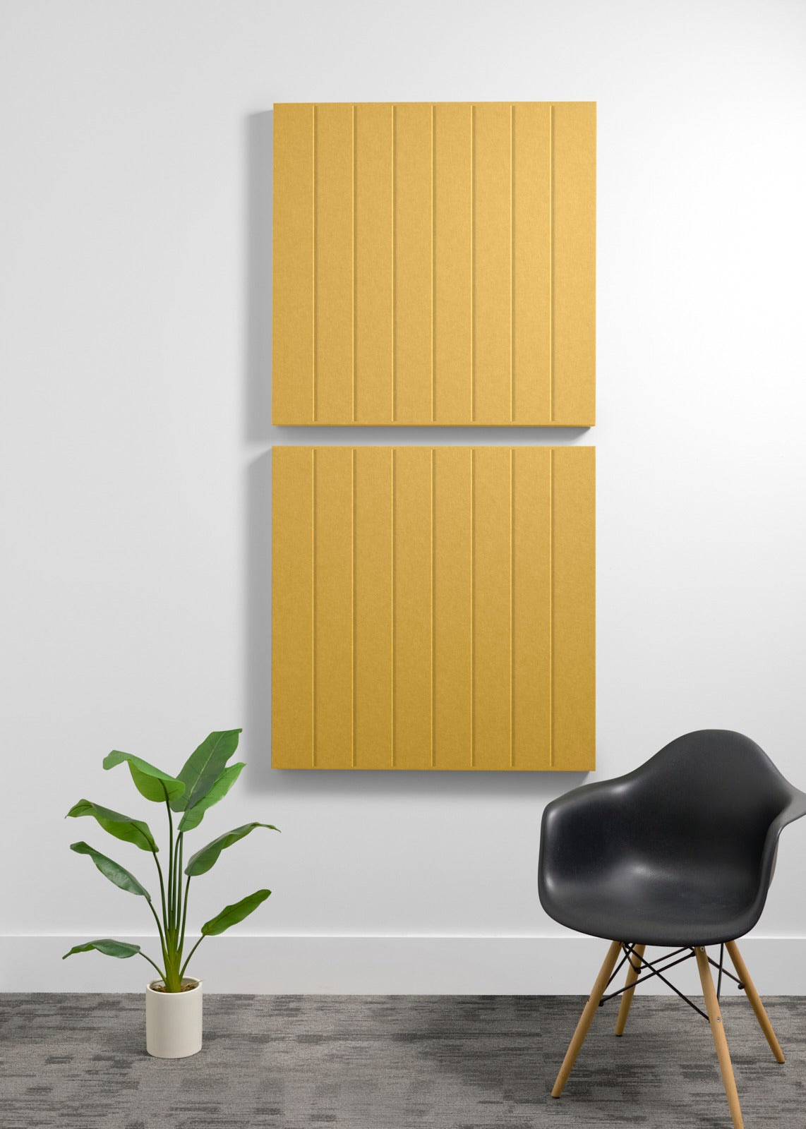Two stacked golden yellow acoustic panels with vertical grooves mounted on a wall above a black chair and potted plant.