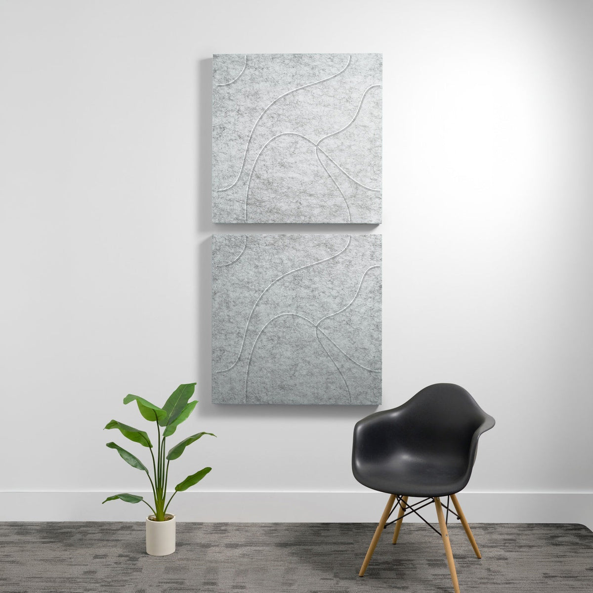 Two stacked gray acoustic panels with topographic line engravings mounted on white wall above black chair and potted plant.