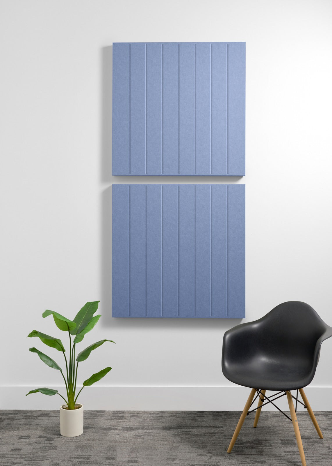 Two blue acoustic wall panels with vertical ribbed texture mounted on white wall above chair and plant.