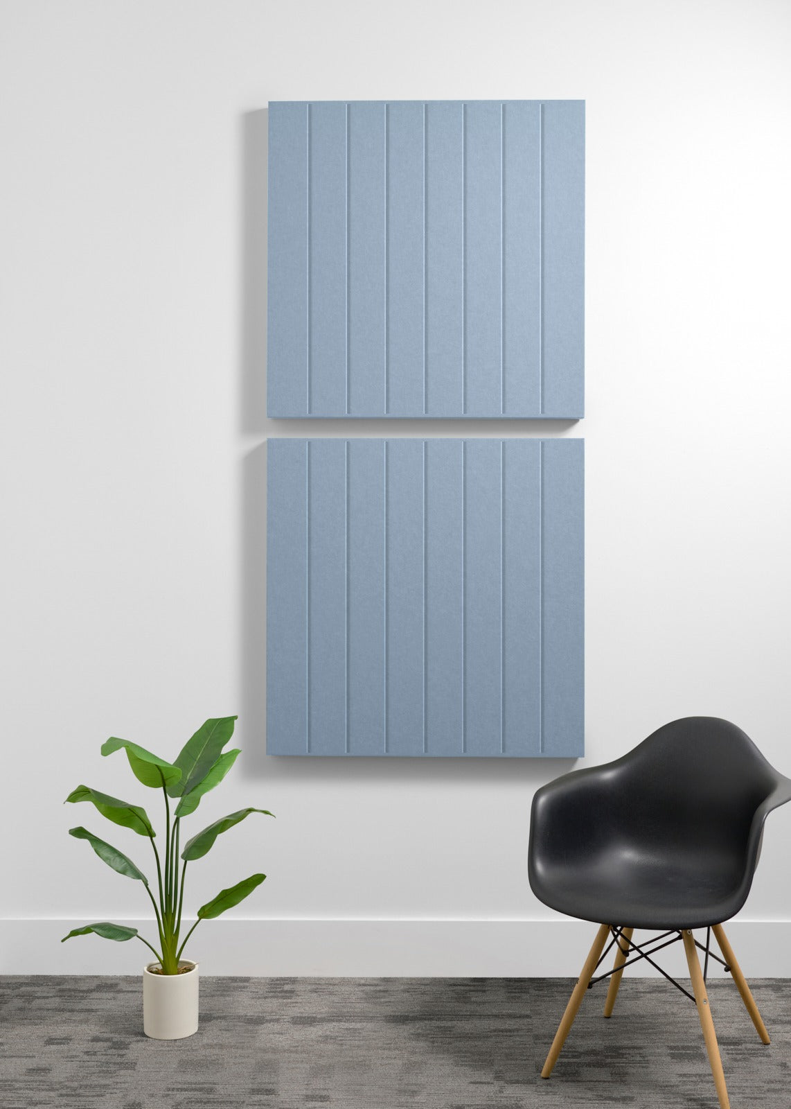 Two blue-gray 3D acoustic panels with vertical ribbed texture mounted on white wall above black chair.