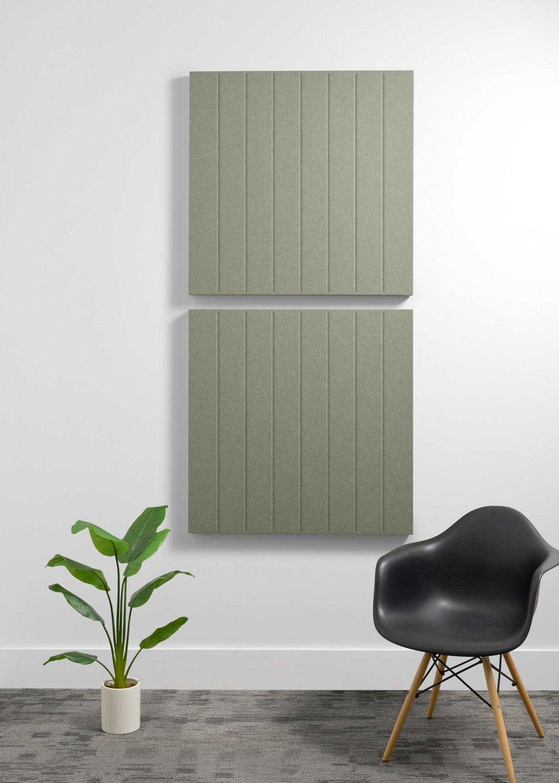 Two large sage green acoustic panels with vertical ribbed texture mounted on wall above black chair and potted plant.