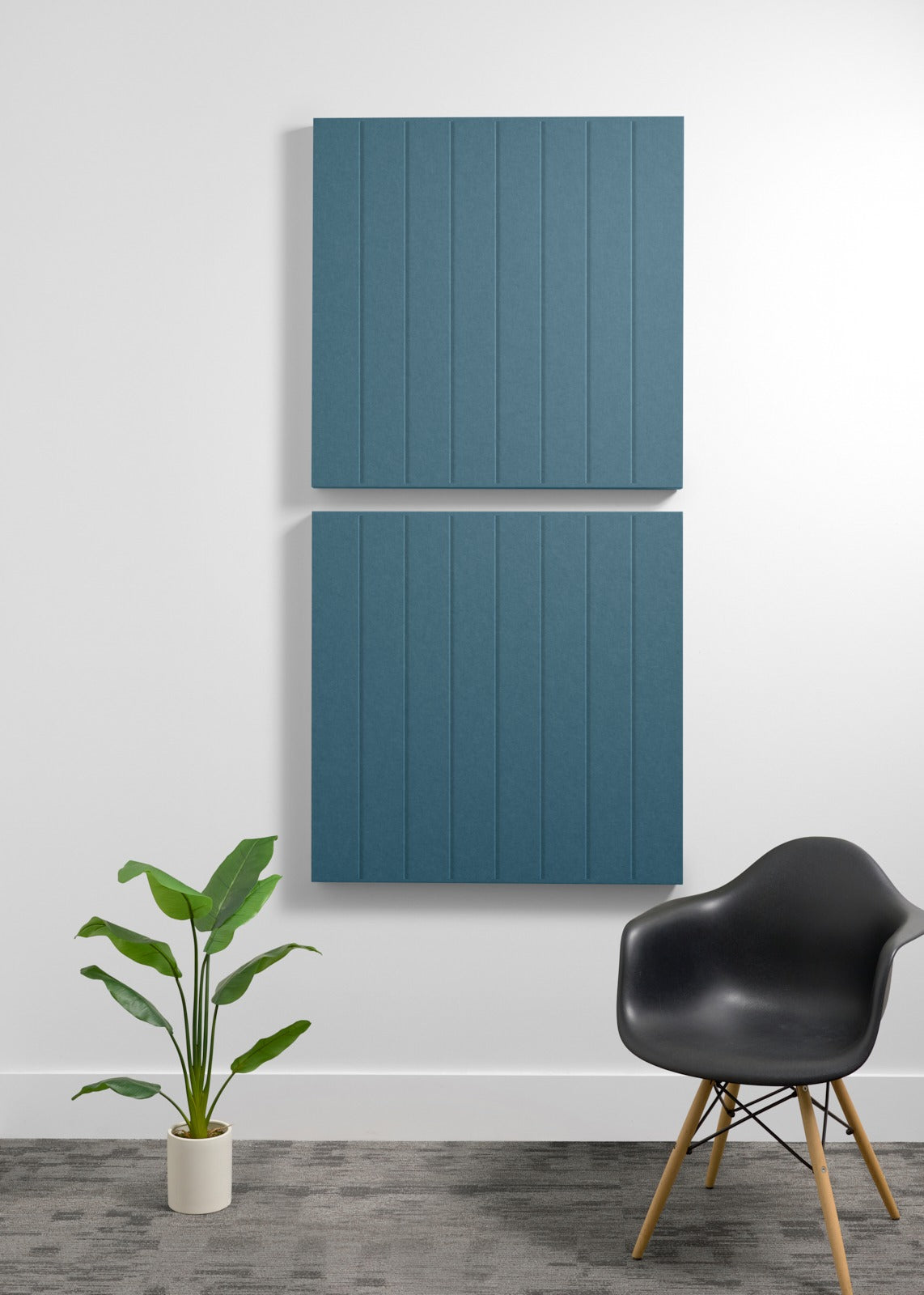Two large teal acoustic wall panels with vertical ribbed texture mounted on a white wall above a black chair and potted plant
