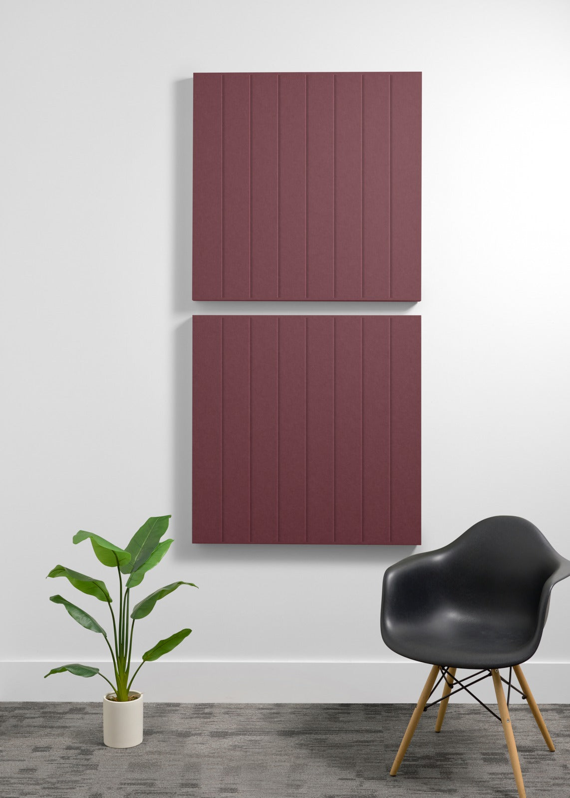 Two burgundy square acoustic panels with vertical ribbed texture mounted on white wall above black chair and potted plant.