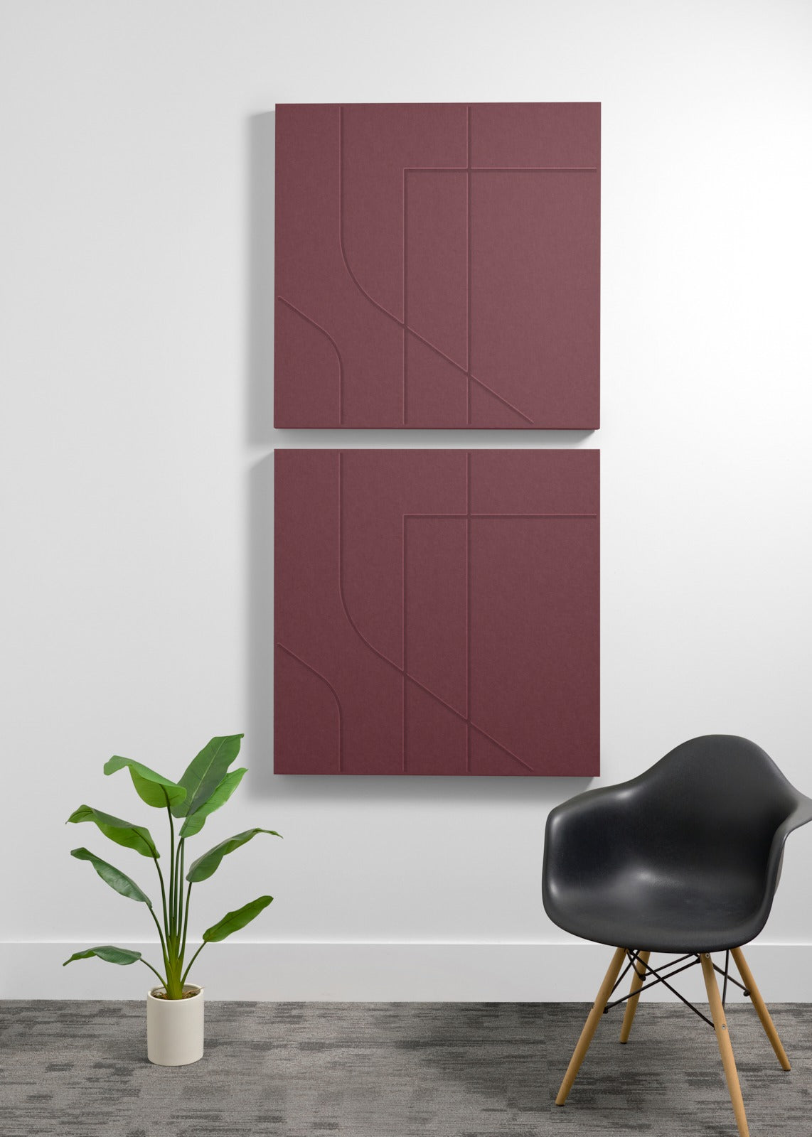 Two maroon red square wall-mounted panels with engraving on a white wall with a black chair and plant in the foreground.
