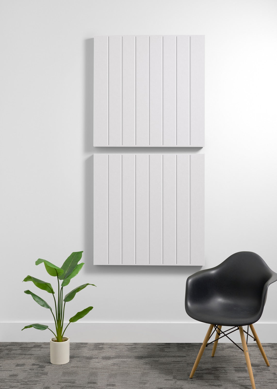 Two white 3D acoustic wall panels with vertical ribbed texture mounted on white wall above black chair and potted plant.
