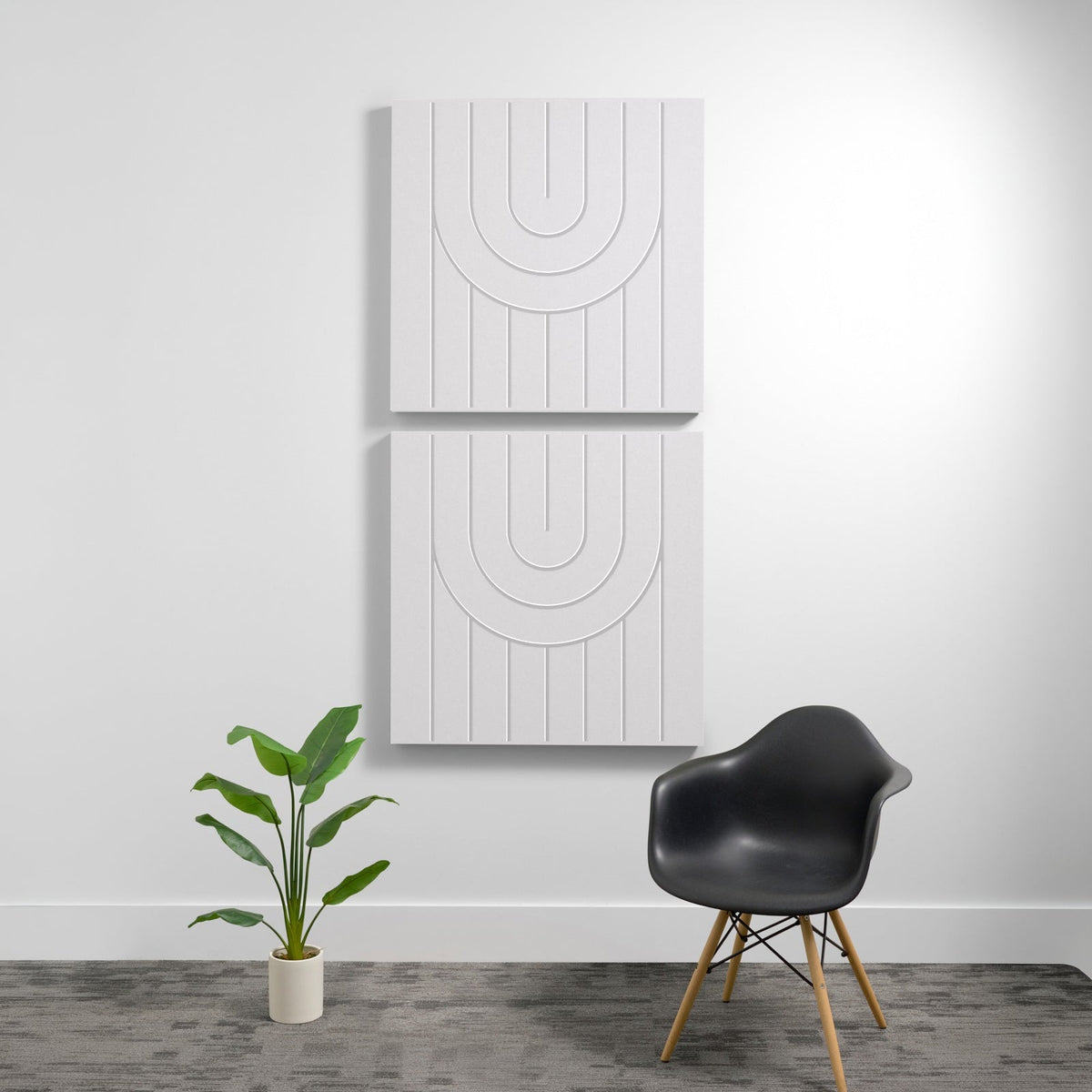 Two white square acoustic panels with vertical ribbing and engraved semicircle design mounted on wall above black chair and p
