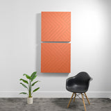 Two stacked orange acoustic wall panels with diagonal line engraving pattern mounted on white wall.