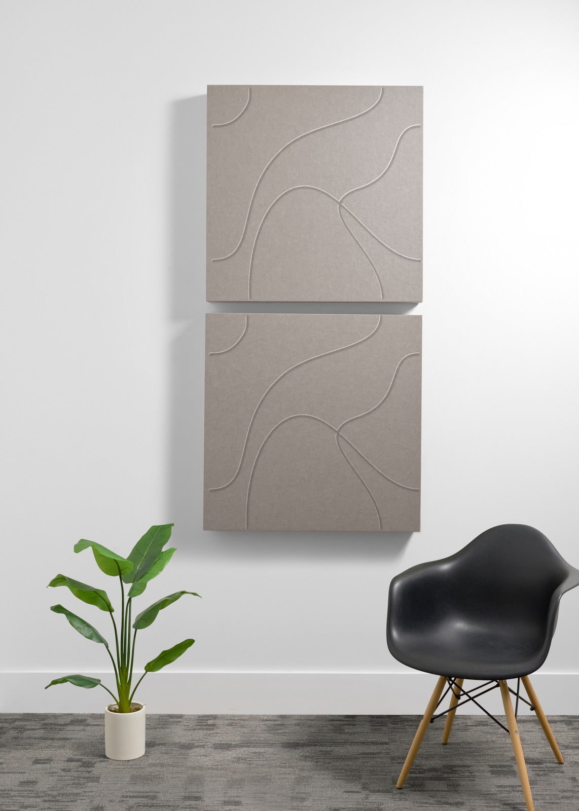 Two stacked beige acoustic panels with engraved topographic line patterns mounted on wall above chair and plant.