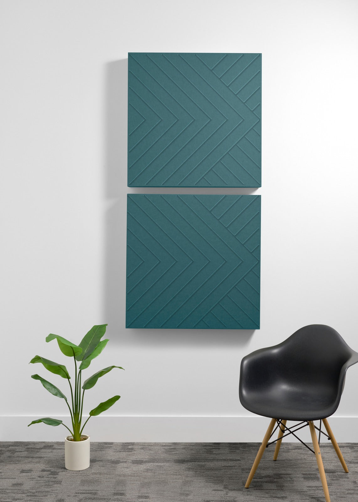 Two teal acoustic panels with engraved chevron pattern mounted vertically on white wall above potted plant and black chair.