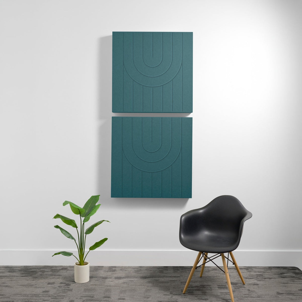 Two teal acoustic wall panels with engraved concentric arc patterns mounted vertically above a black chair and potted plant.