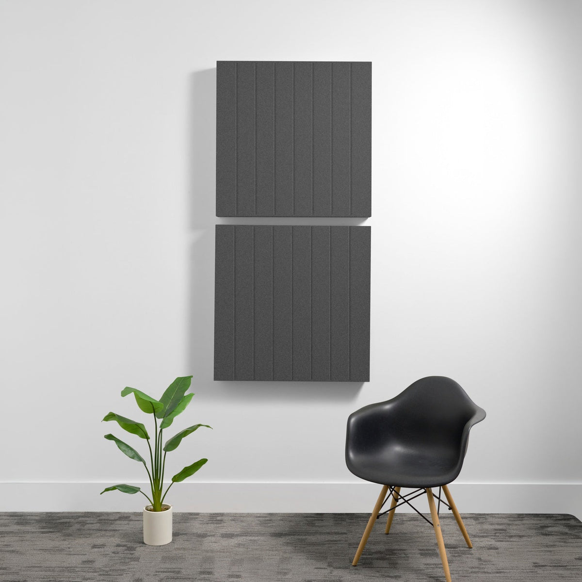 Two large dark gray acoustic panels with parallel vertical engraved lines mounted on wall above chair and plant.