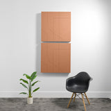 Two stacked terracotta acoustic panels with engraved geometric line patterns mounted on a white wall.