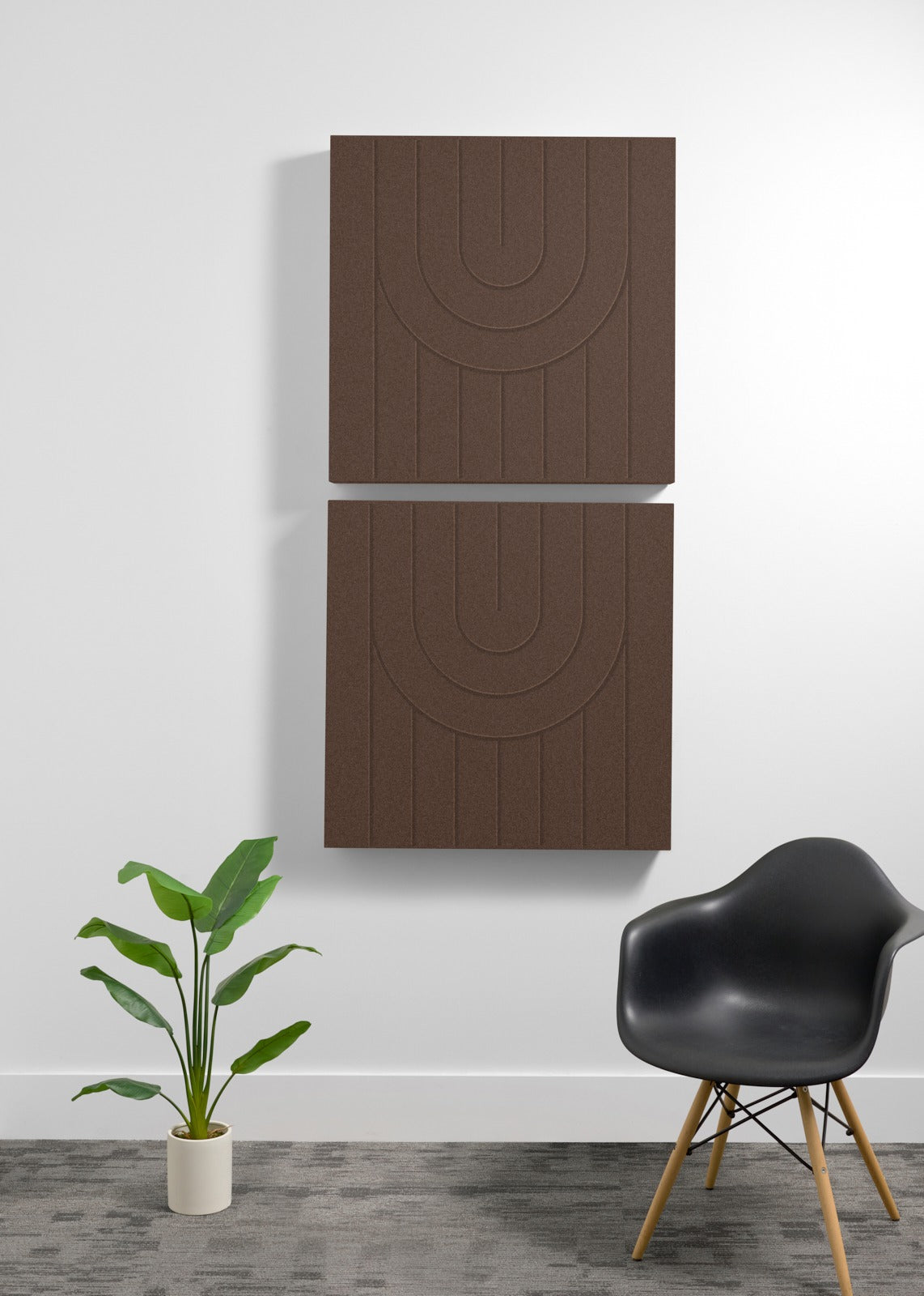 Two brown acoustic panels with engraved arch pattern mounted vertically on wall above black chair and potted plant.