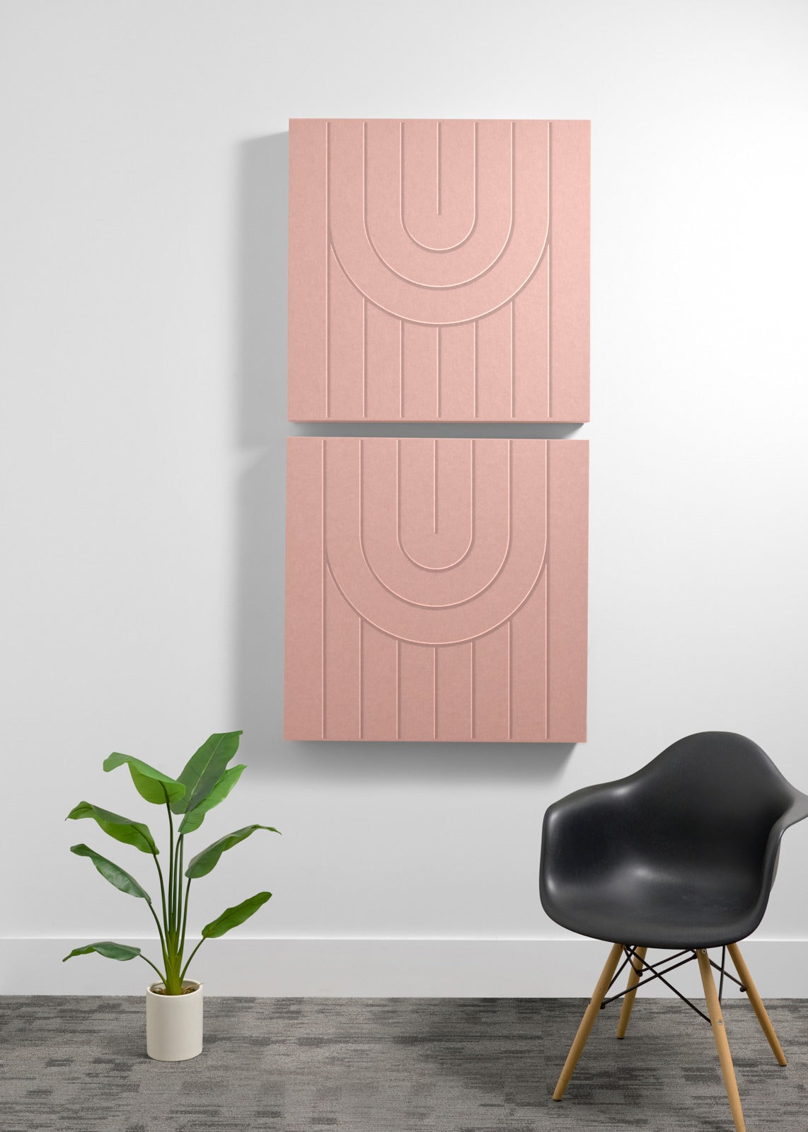 Two stacked pink acoustic panels with engraved arch patterns mounted on a wall above a black chair and potted plant.