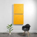 Two stacked yellow acoustic boxes with engraved topographic line patterns mounted on white wall.