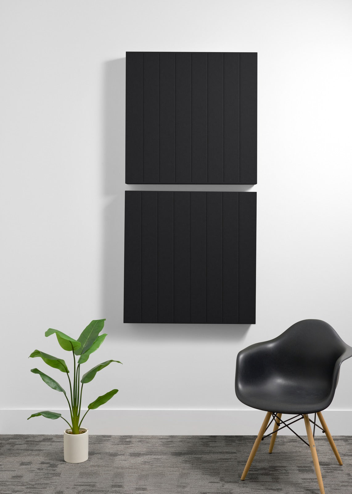 Two black square acoustic panels with parallel engraved lines mounted vertically on a white wall.