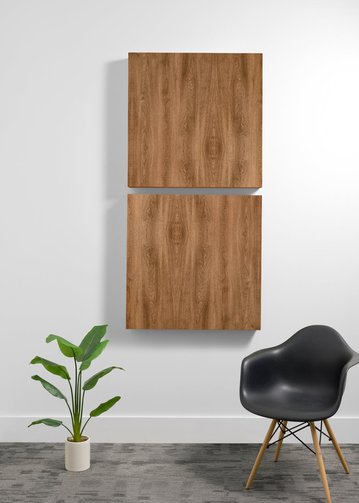 Two square wood wall art panels hanging vertically on a white wall in a modern room setting, with a black chair and a potted green plant below.