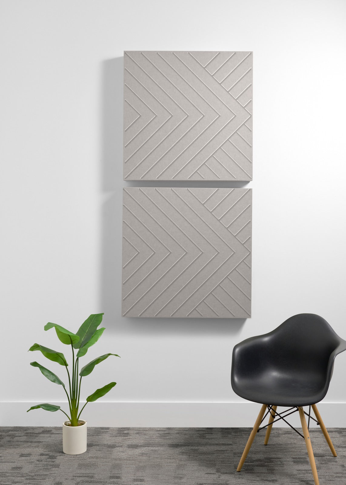 Two stacked light gray acoustic panels with engraved chevron pattern mounted on wall above chair and plant.