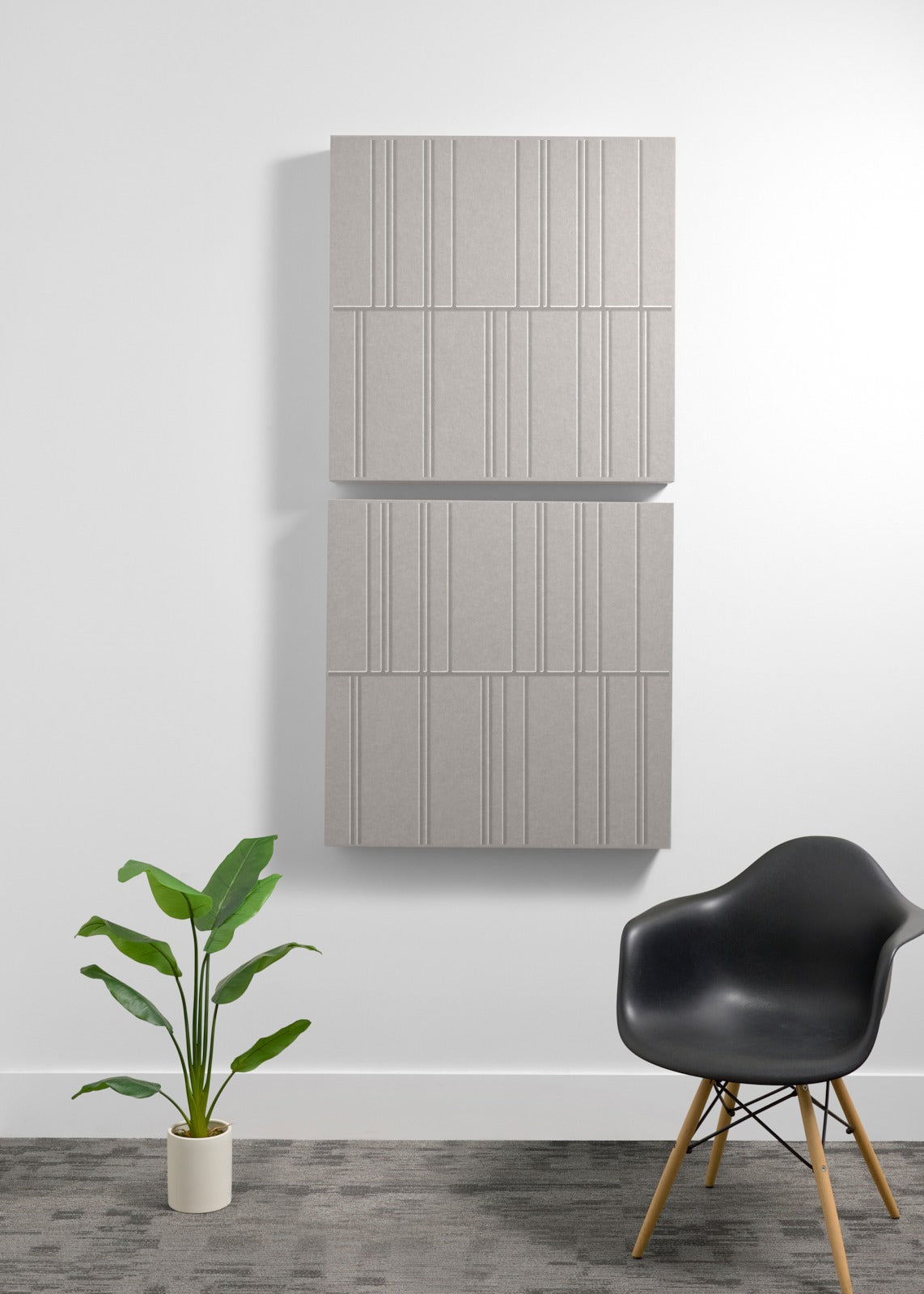 Four stacked gray acoustic boxes with vertical engraved line patterns mounted on a white wall above a black chair and potted 