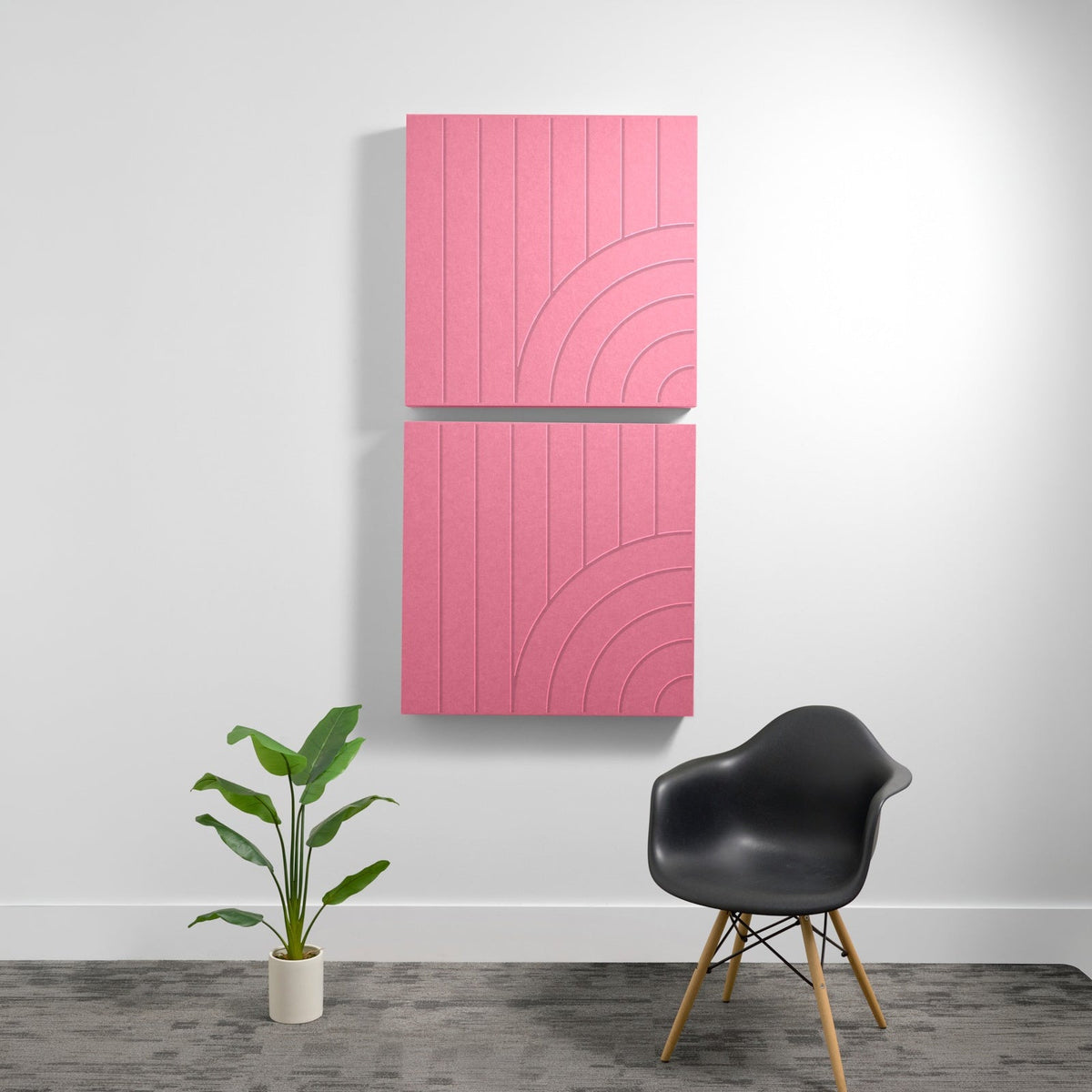 Two stacked pink acoustic panels with engraved curved line patterns mounted on white wall above black chair and potted plant.