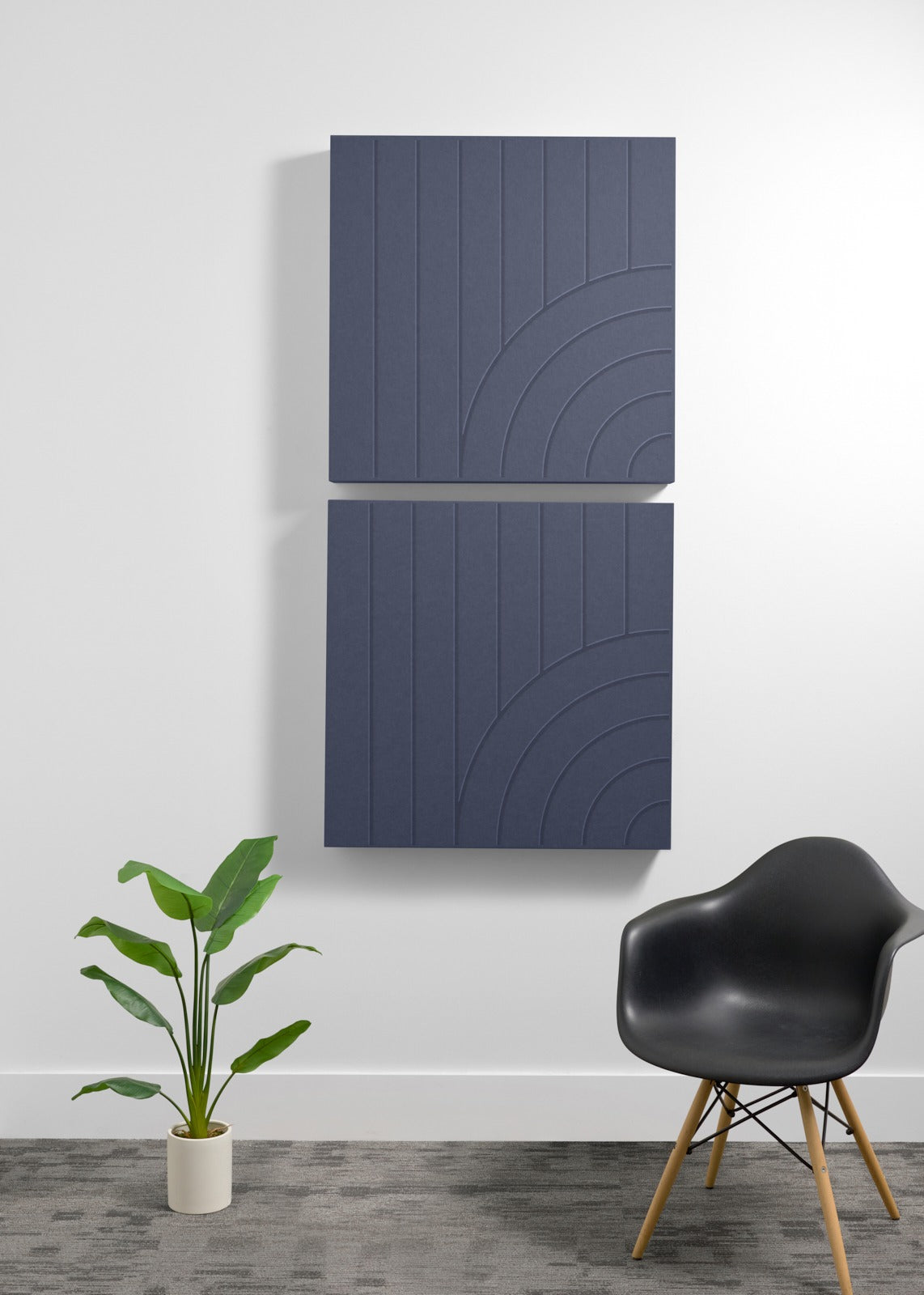 Two dark blue square acoustic panels with vertical lines and curved geometric engravings mounted on a white wall.