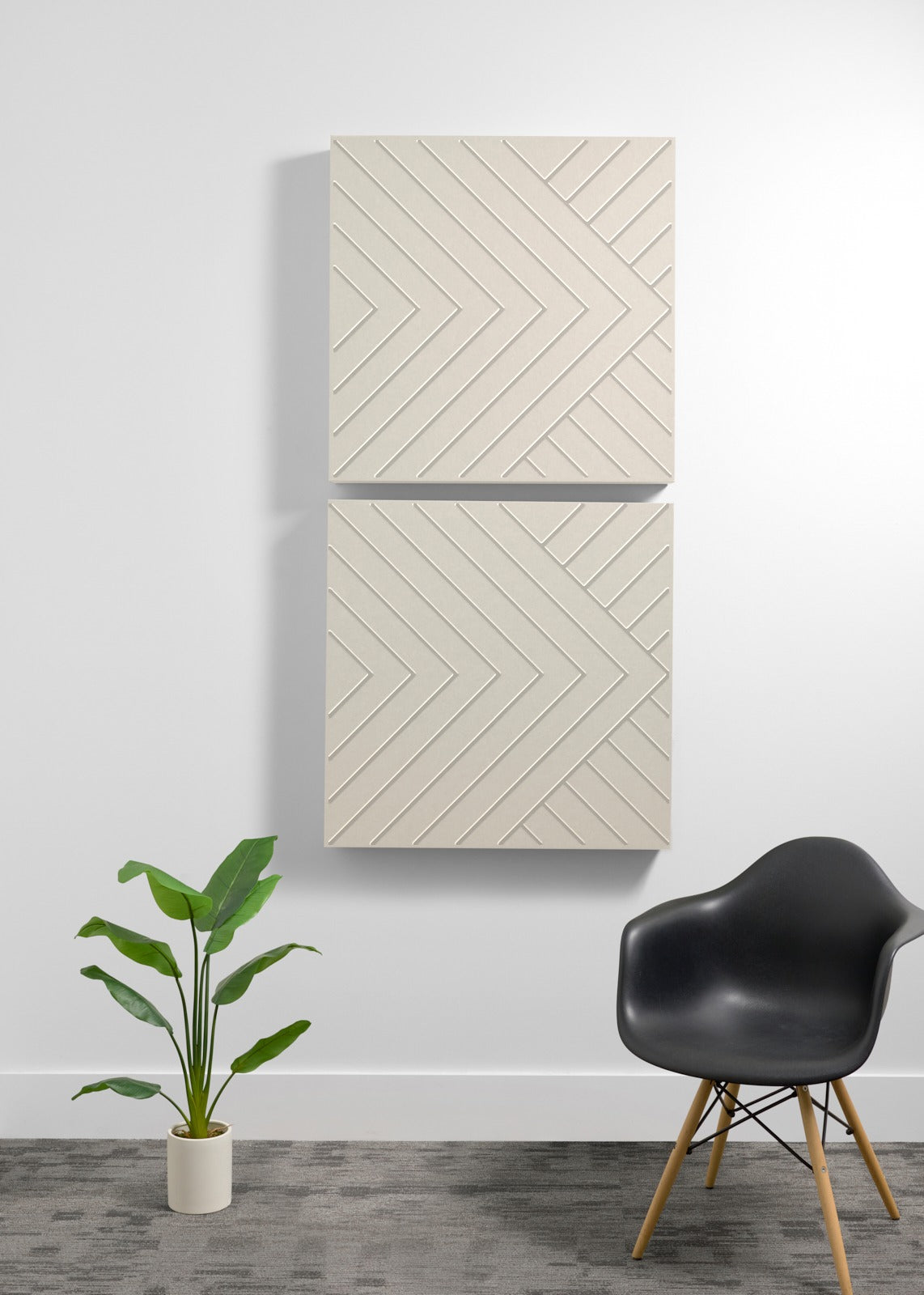 Two stacked cream-colored acoustic wall panels with engraved chevron pattern, displayed above a black chair and potted plant.