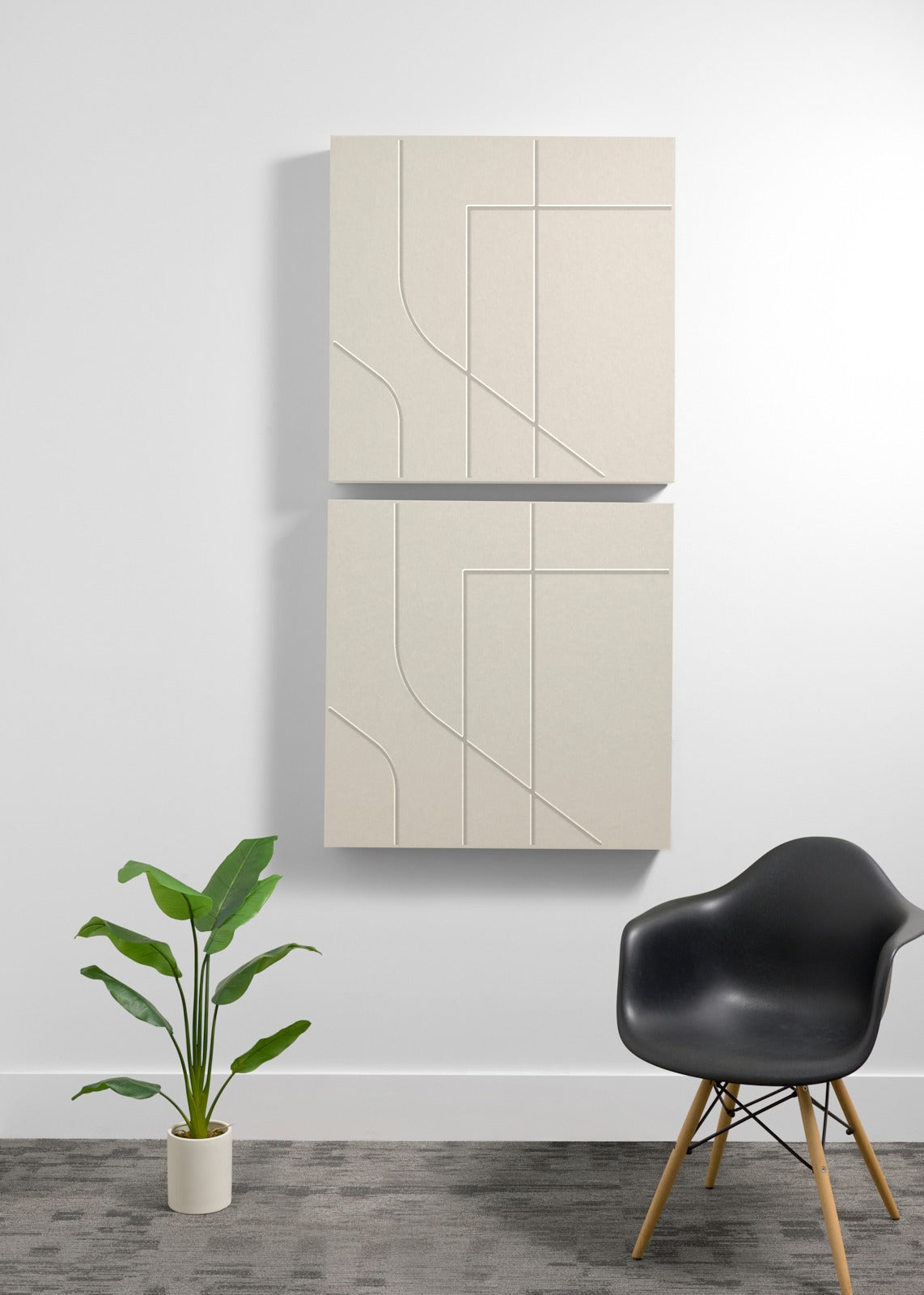 Two ivory white square wall-mounted panels with engraving on a white wall with a black chair and plant in the foreground.