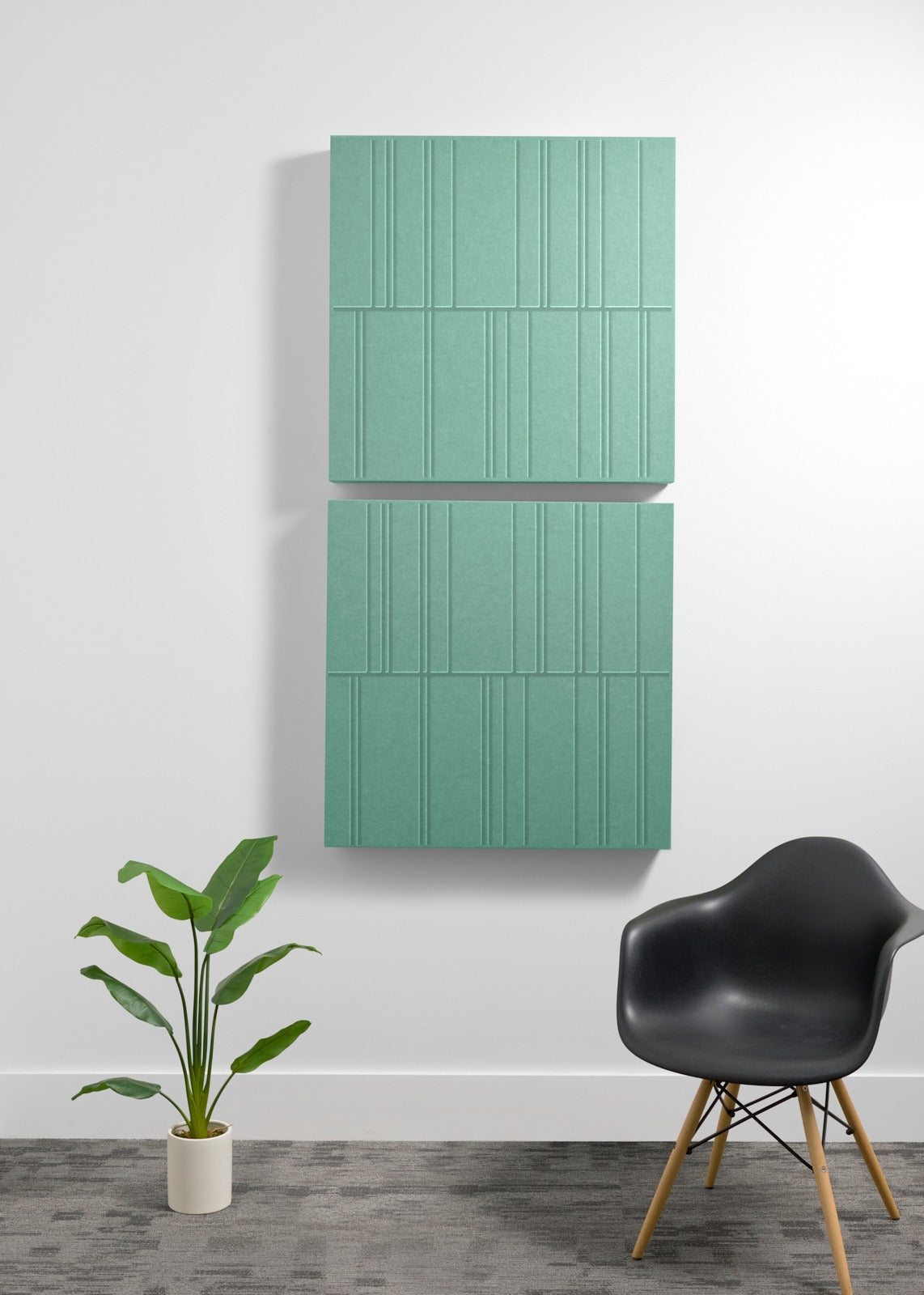 Four sage green acoustic panels with engraved linear pattern mounted vertically on wall above black chair and potted plant.