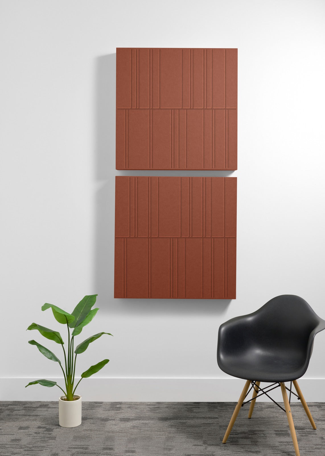 Two stacked terracotta-colored acoustic panels with engraved linear pattern mounted on white wall above black chair and potte