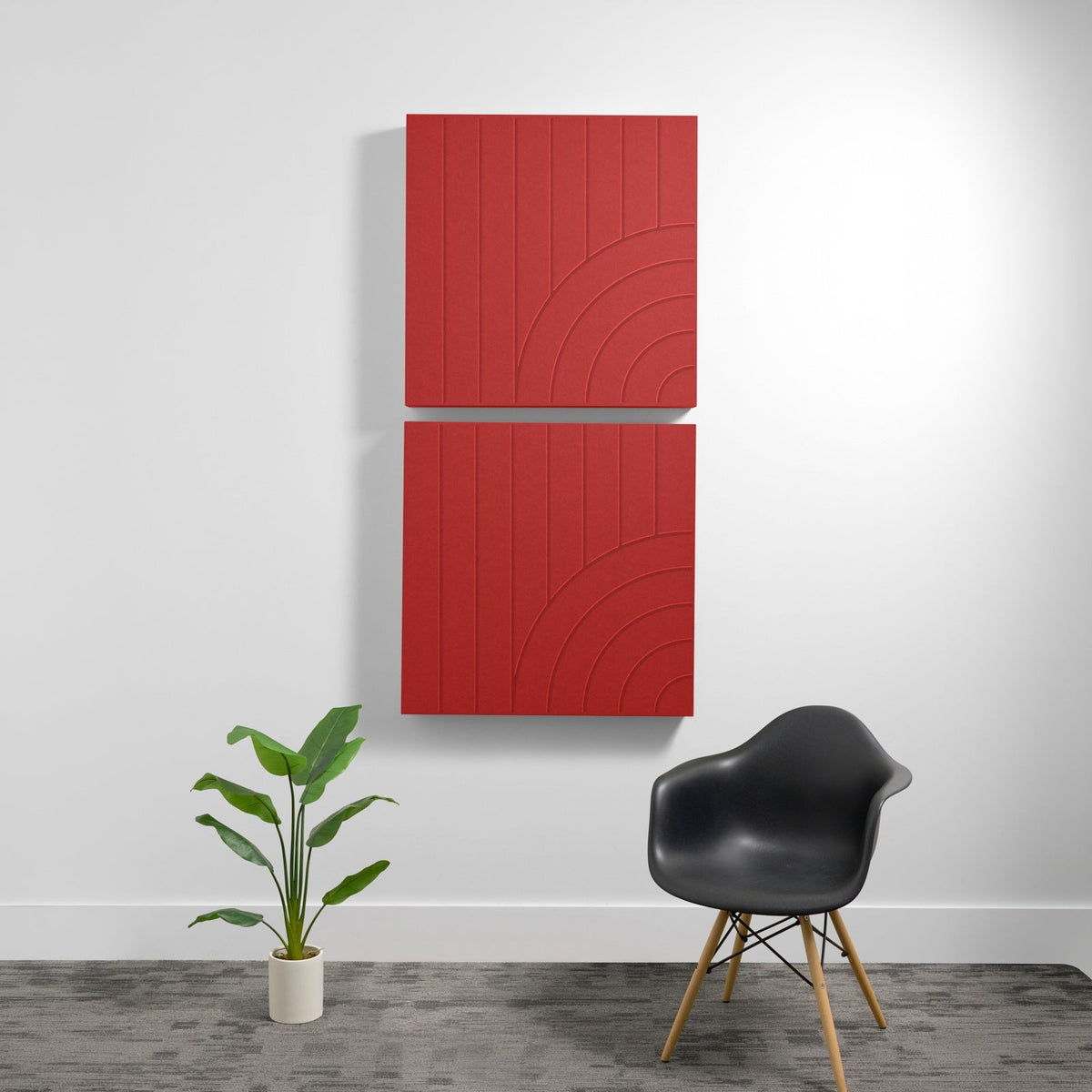Two red acoustic panels with engraved tangent arc design mounted on white wall above black chair and potted plant.