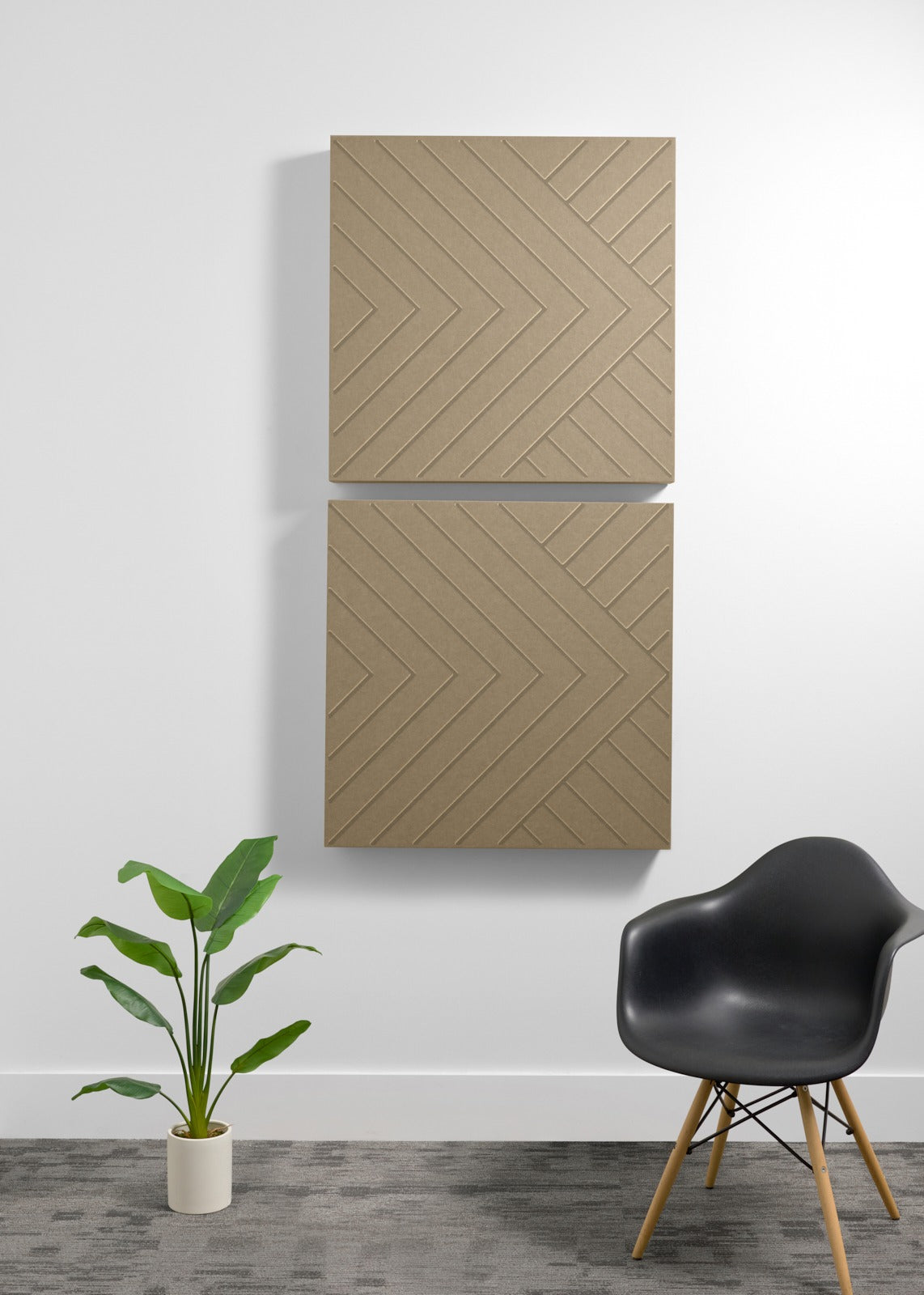 Two stacked tan acoustic panels with engraved chevron pattern mounted on wall above potted plant and black chair.