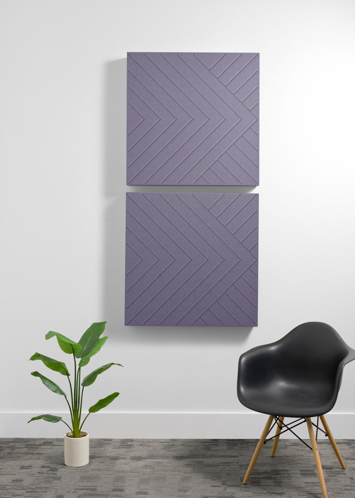 Two stacked purple acoustic panels with engraved geometric chevron pattern mounted on wall above chair and plant.