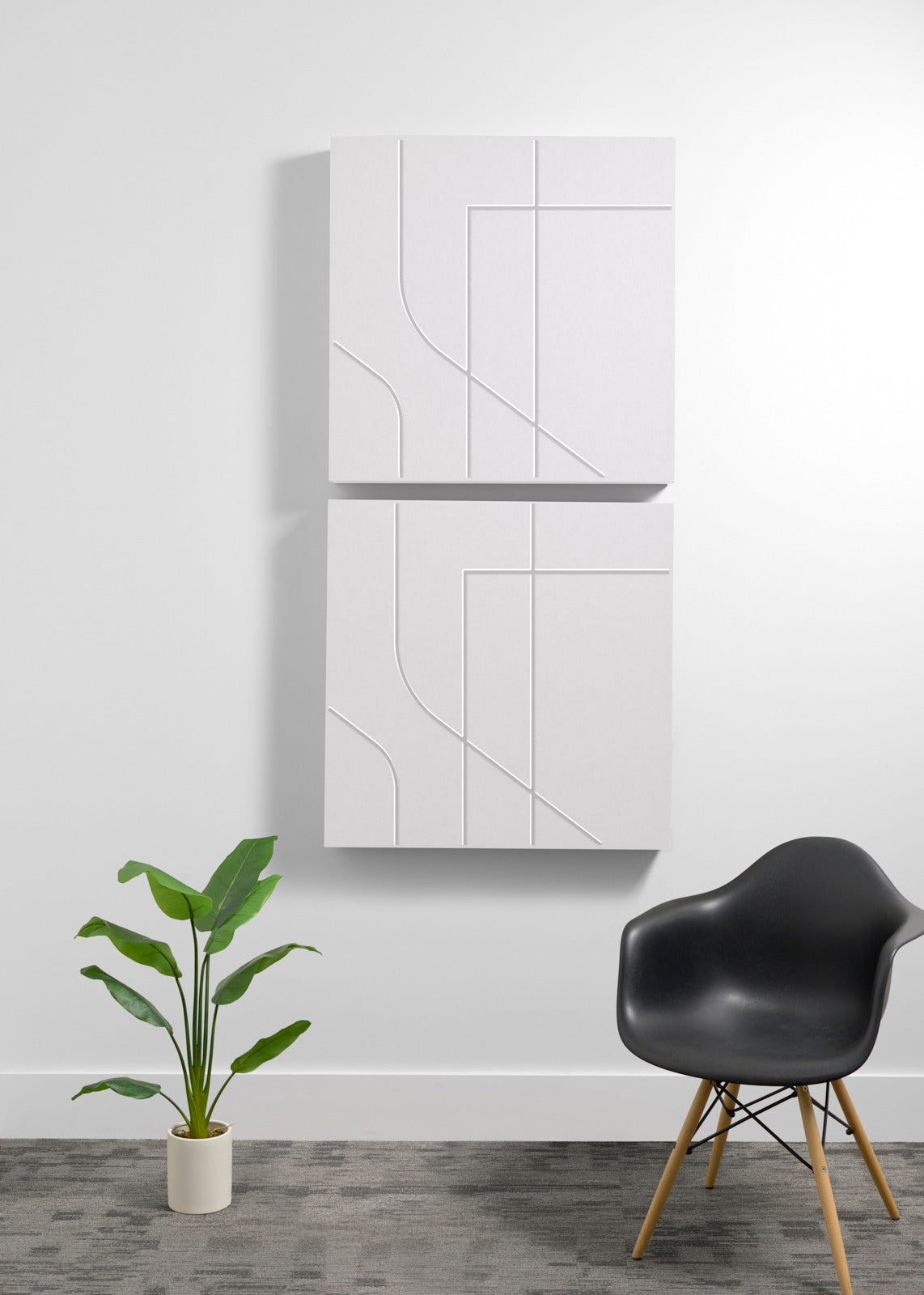 Two white square wall-mounted panels with engraving on a white wall with a black chair and plant in the foreground.