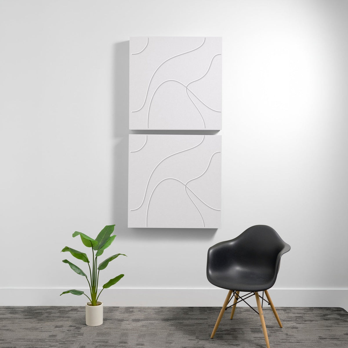 Two stacked white acoustic wall panels with topographic line engravings, mounted vertically above a black chair and potted pl
