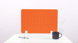 Orange grid desk divider with rounded corners standing on white desk surface next to coffee mug and pens.