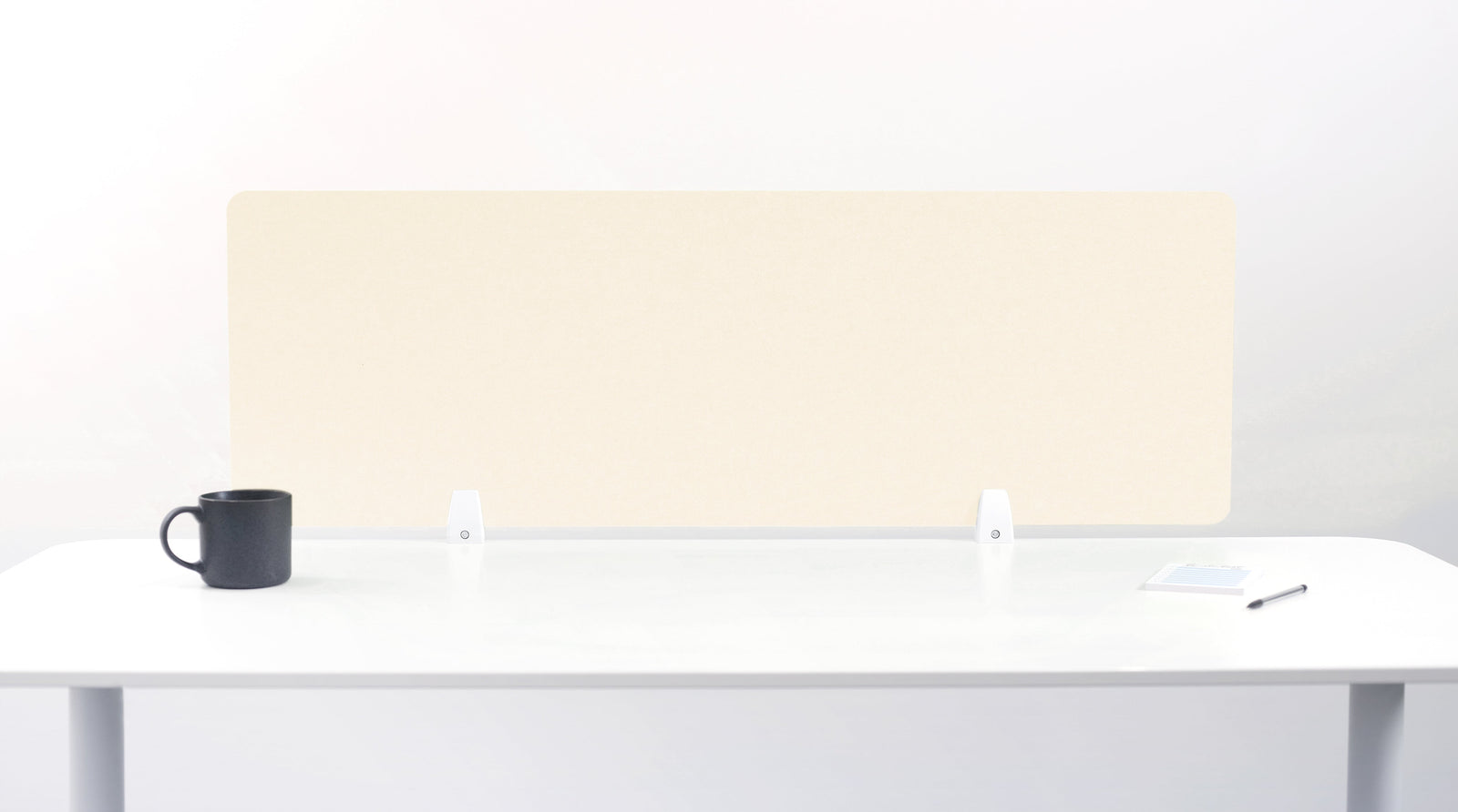 An ivory-colored felt desk divider placed on a white desk with a black mug and a pen beside it.