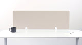 Beige rectangular desk divider with white mounting brackets positioned on white desk surface.