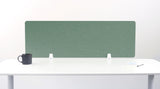 Sage green fabric desk divider with white mounting brackets on white desk surface.