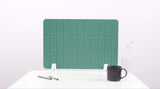Green grid desk divider with vertical panels and white support feet on white desk surface.