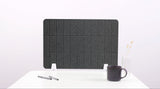 Dark gray grid-patterned desk divider with white feet, positioned on white surface with mug and pen holder.