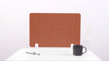 Terracotta grid-patterned desk divider with white base supports, displayed on white desk with mug and pens.