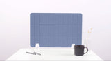 Blue grid desk divider with white mounting brackets, positioned on white desk with coffee mug and pens.